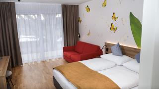 Sie sehen ein Doppelzimmer superior im neuen JUFA Hotel Bad Radkersburg mit komfortablen Boxspringbett, Couch und Balkon.