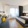 Sie sehen ein Doppelbett und eine Couch im JUFA Hotel Hamburg HafenCity. Der Ort für erlebnisreichen Städtetrip für die ganze Familie und der ideale Platz für Ihr Seminar.