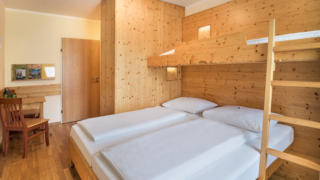 Sie sehen ein Doppelbett mit Kinderbett im JUFA Hotel Bad Aussee***. Der Ort für tollen Sommerurlaub an schönen Seen für die ganze Familie.