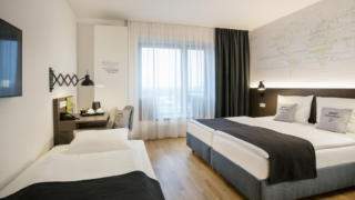 Sie sehen ein Doppelbett und Einzelbett mit Kissen im JUFA Hotel Hamburg HafenCity. Der Ort für erlebnisreichen Städtetrip für die ganze Familie und der ideale Platz für Ihr Seminar.