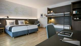 Sie sehen ein Doppelbett im Vierbettzimmer im JUFA Hotel Hamburg HafenCity. Der Ort für erlebnisreichen Städtetrip für die ganze Familie und der ideale Platz für Ihr Seminar.