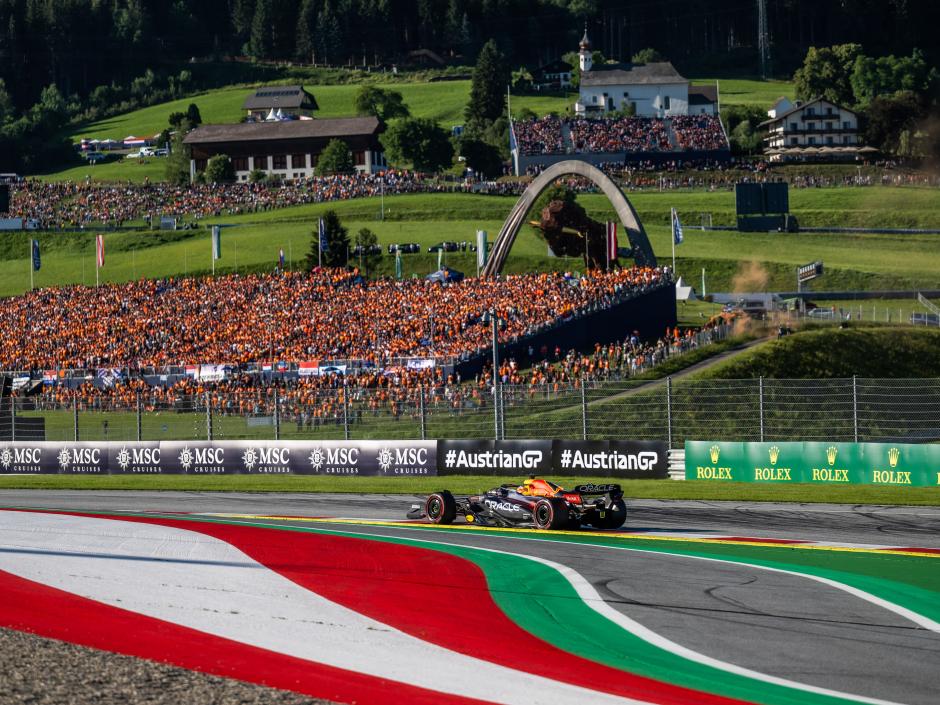 Sie sehen ein Bild vom Formel 1 Rolex Großen Preis von Österreich am Red Bull Ring in Spielberg mit dem Formel 1 Auto von Max Verstappen und zahlreichen Zuschauer im Hintergrund.
