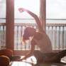 Eine junge Frau sitzt vor einem Fenster im Schneidersitz am Boden und macht eine Yogaübung. JUFA Hotels bietet erholsamen Thermen- und Badespass für die ganze Familie.