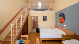 Sie sehen ein Galeriezimmer für fünf Personen im JUFA Hotel Nördlingen. Der Ort für kinderfreundlichen und erlebnisreichen Urlaub für die ganze Familie.