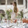Sie sehen eine gedeckte Hochzeitstafel mit einer Braut im Atrium des JUFA Hotel Schloss Röthelstein/Admont***. Der Ort für märchenhafte Hochzeiten und erfolgreiche und kreative Seminare.