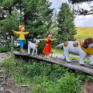 Sie sehen Peter, ein Lamm, Heidi und einen großen Hund aus der bekannten Kinder Zeichentrickserie"Heidi" als Figuren, die über einen Holzbalken balancieren. JUFA Hotels bietet erholsamen Ski- und Wanderurlaub für Familien in Kärnten.