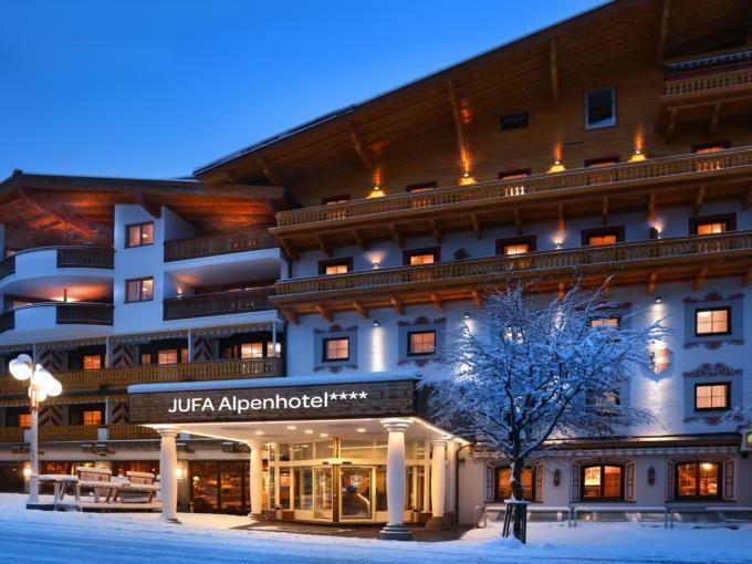 Sie sehen eine Außenansicht vom JUFA Alpenhotel Saalbach**** am Abend im Winter. JUFA Hotels bietet erholsamen Familienurlaub und einen unvergesslichen Winterurlaub.