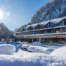 Sie sehen eine Außenansicht vom JUFA Hotel Almtal mit Sonnenschein im Winter. JUFA Hotels bietet erholsamen Familienurlaub und einen unvergesslichen Winterurlaub.