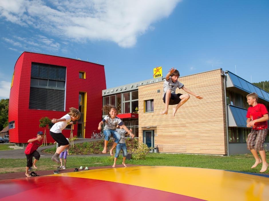 Sie sehen eine Außenansicht vom JUFA Hotel Bleiburg/Pliberk – Sport-Resort mit Kindern im Sommer. JUFA Hotels bietet Ihnen den Ort für erfolgreiches Training in ungezwungener Atmosphäre für Vereine und Teams.