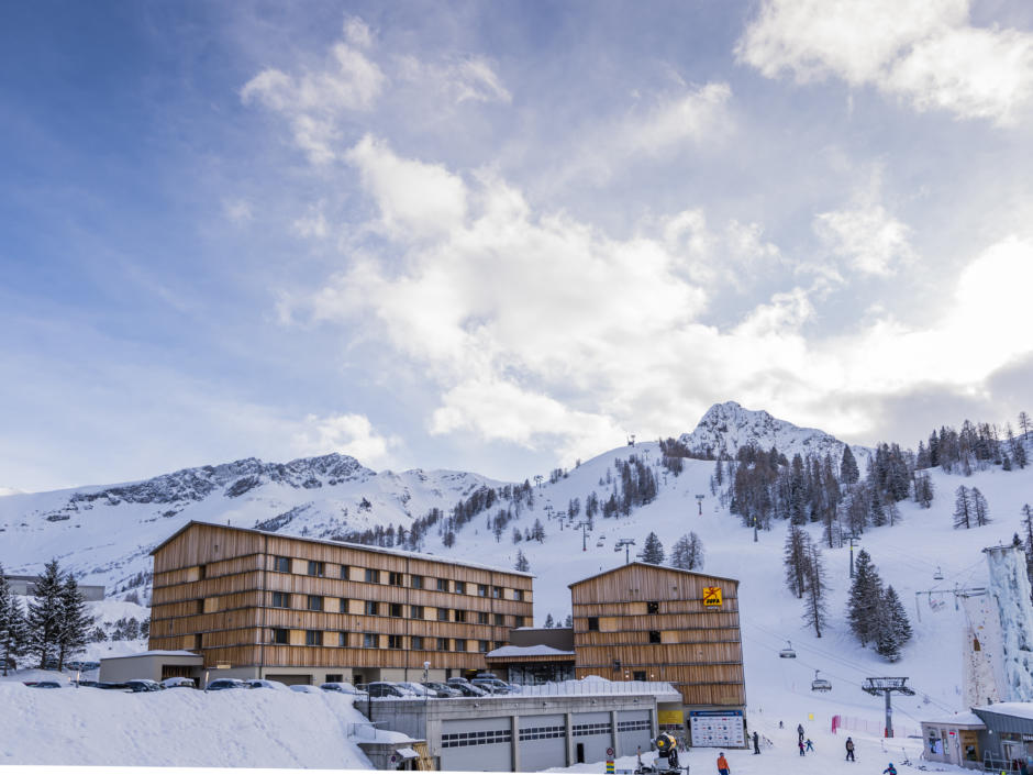 Sie sehen eine Außenansicht vom JUFA Hotel Malbun – Alpin-Resort*** mit Piste im Winter. JUFA Hotels bietet erholsamen Familienurlaub und einen unvergesslichen Winterurlaub.