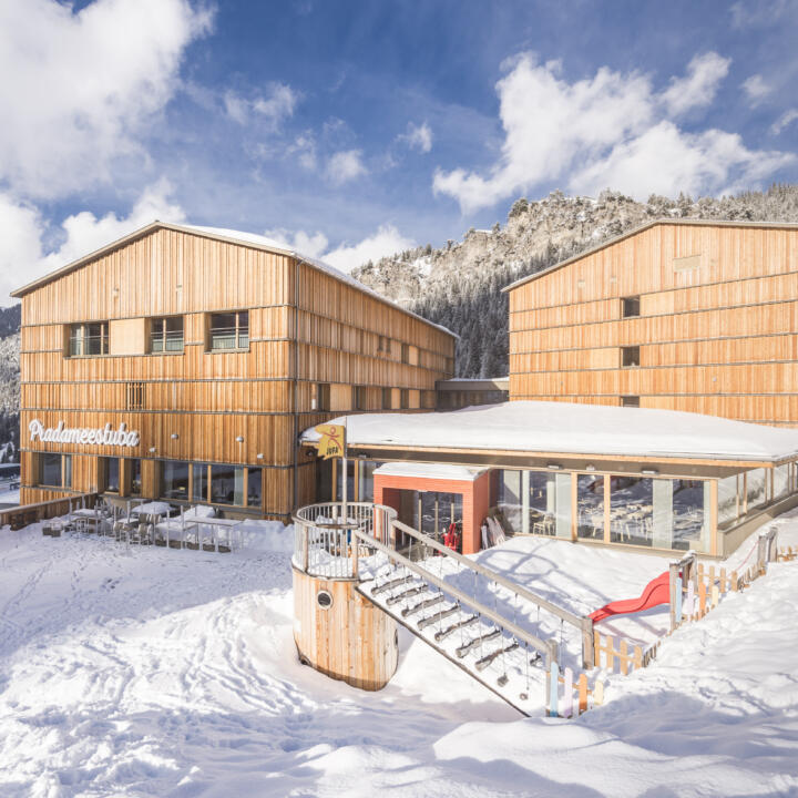 Sie sehen eine Außenansicht vom JUFA Hotel Malbun – Alpin-Resort*** mit Spielplatz im Winter. JUFA Hotels bietet erholsamen Familienurlaub und einen unvergesslichen Winterurlaub.