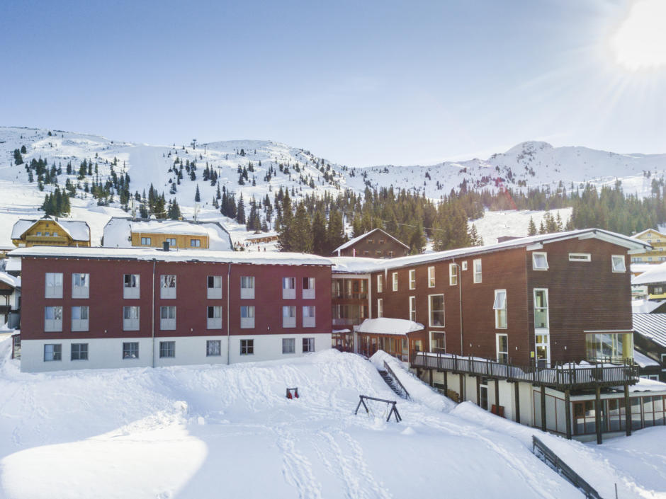 Sie sehen eine Außenansicht vom JUFA Hotel Planneralm – Alpin-Resort*** mit Bergblick im Winter. JUFA Hotels bietet erholsamen Familienurlaub und einen unvergesslichen Winterurlaub.