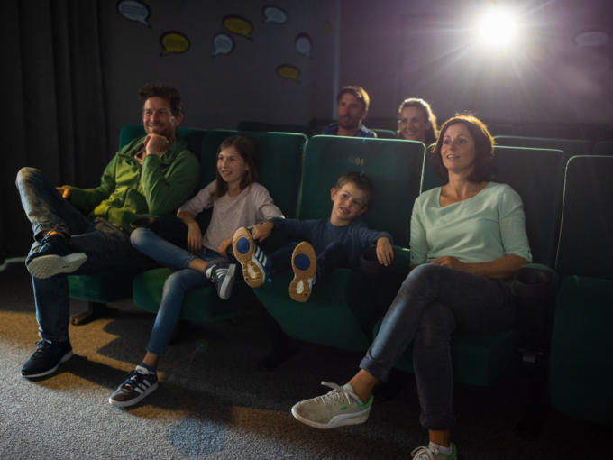 Sie sehen eine Familie im hoteleigenen Kino im JUFA Kempten. Der Ort für kinderfreundlichen und erlebnisreichen Urlaub für die ganze Familie.