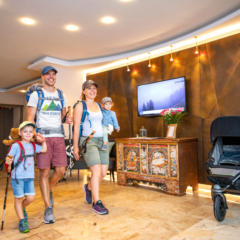 Sie sehen eine Familie in der Lobby des JUFA Alpenhotel Saalbach****, die zum Wandern aufbricht. JUFA Hotels bietet erholsamen Familienurlaub und einen unvergesslichen Winter- und Wanderurlaub.