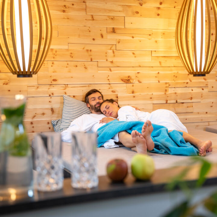 Sie sehen ein Paar, das sich im Ruhebereich der Wellnessanlage des JUFA Alpenhotel Saalbach**** entspannt. JUFA Hotels bietet erholsamen Familienurlaub und einen unvergesslichen Winter- und Wanderurlaub.