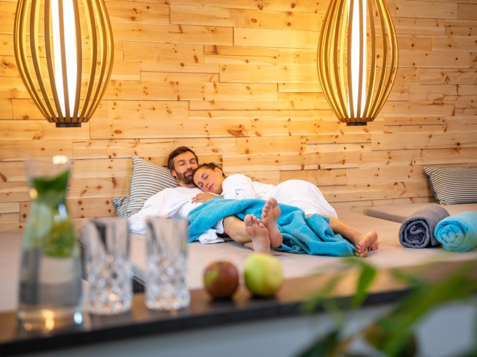 Sie sehen ein Paar, das sich im Ruhebereich der Wellnessanlage des JUFA Alpenhotel Saalbach**** entspannt. JUFA Hotels bietet erholsamen Familienurlaub und einen unvergesslichen Winter- und Wanderurlaub.
