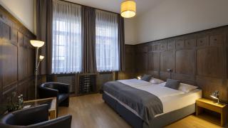 Sie sehen ein Doppelbett und zwei Lehnsessel in einem holzvertäfelten Raum im Appartement für 4 Personen im JUFA Hotel Bregenz am Bodensee. Der Ort für einen unvergesslichen Wander-, Rad- und Kultururlaub für Familien, Freunde und Paare.