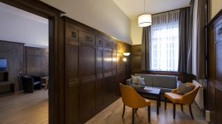 Sie sehen eine Sitzecke mit Sofa, Sofatisch und zwei Lehnsesseln in einem holzvertäfelten Raum im Appartement für 4 Personen im JUFA Hotel Bregenz am Bodensee. Der Ort für einen unvergesslichen Wander-, Rad- und Kultururlaub für Familien, Freunde und Paare.