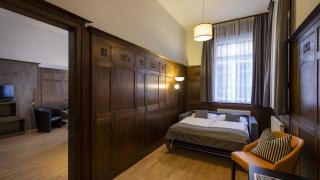Sie sehen ein Sofa-Doppelbett in einem holzvertäfelten Raum im Appartement für 4 Personen im JUFA Hotel Bregenz am Bodensee. Der Ort für einen unvergesslichen Wander-, Rad- und Kultururlaub für Familien, Freunde und Paare.