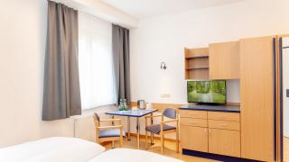 Sie sehen ein Bild vom Doppelzimmer im JUFA Hotel Garni Stubenberg in der Oststeiermark mit Kasten, Fernseher und Sitzmöglichkeiten.