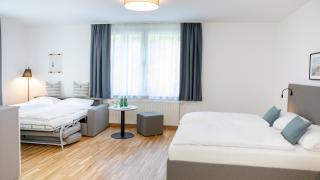 Sie sehen ein Bild vom Family & Friends Zimmer im JUFA Hotel Garni Stubenberg in der Oststeiermark mit ausgezogener Schlafcouch und Sitzecke.