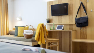 Sie sehen einen Ausschnitt von einem Doppelzimmer im JUFA Hotel im Weitental / Bruck a.d. Mur. Über dem Sessel hängt eine gelbe Jacke. JUFA Hotels bietet erholsamen Familienurlaub und einen unvergesslichen Winter- und Wanderurlaub.