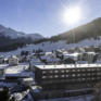Sie sehen eine Winter Außenaufnahme mit Sonnenschein vom JUFA Hotel Savognin. Der Ort für erholsamen Ski- und Wanderurlaub für Familien.