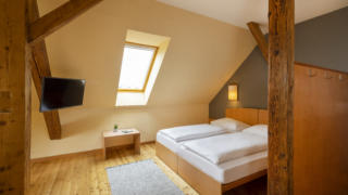 Sie sehen ein Doppelbett. So sind die Doppelzimmer und Einzelzimmer im JUFA Klosterhotel Judenburg ausgestattet. Der Ort für erholsamen Familienurlaub und einen unvergesslichen Winter- und Wanderurlaub.