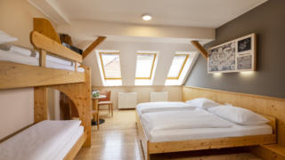 Sie sehen ein Doppelbett und ein Stockbett mit zwei Betten. So sind die Family Friends 4 Zimmer im JUFA Klosterhotel Judenburg ausgestattet. Der Ort für erholsamen Familienurlaub und einen unvergesslichen Winter- und Wanderurlaub.