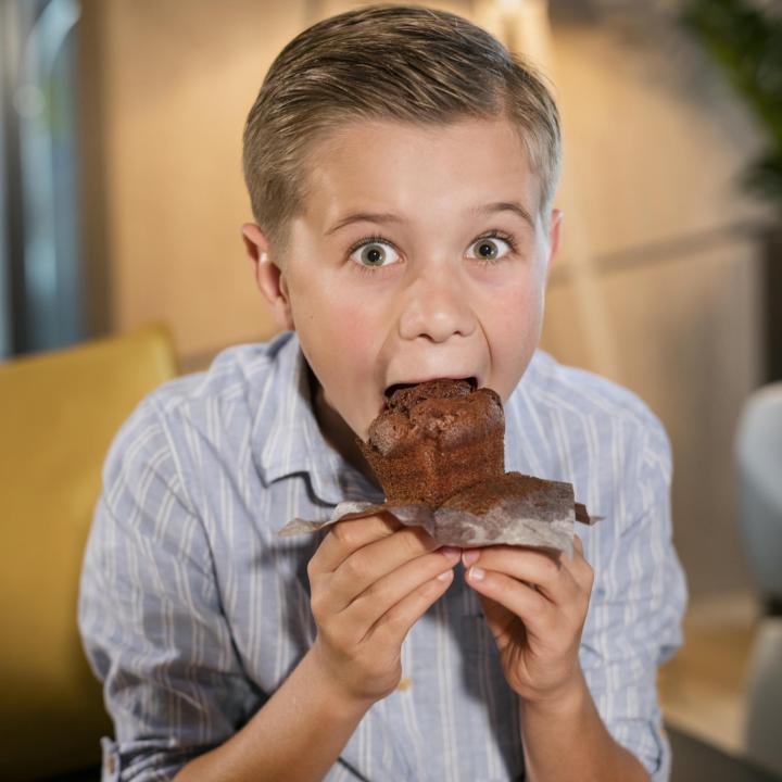Sie sehen einen Jungen mit großen Augen, der einen Muffin isst im JUFA Hotel Weiz. Der Ort für kinderfreundlichen und erlebnisreichen Urlaub für die ganze Familie.