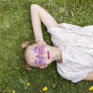 Sie sehen ein Mädchen als Schmetterling geschminkt zufrieden im Gras liegen.