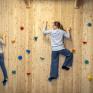 Sie sehen zwei Kinder, die gerade die hölzerne Boulderwand im Indoor-KInderspielbereich im JUFA Hotel Bad Radkersburg erklimmen.