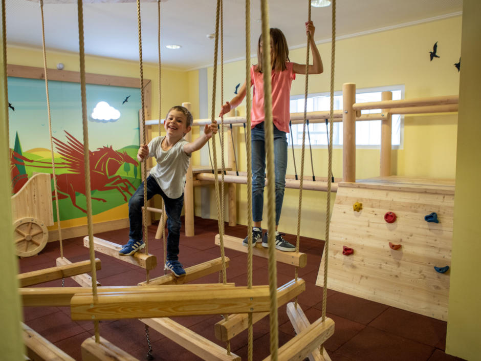 Siesehen einen Jungen und ein Mädchen klettern zwischen Seilen im JUFA Kempten. Der Ort für kinderfreundlichen und erlebnisreichen Urlaub für die ganze Familie.