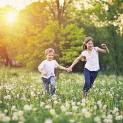 Sie sehen zwei Kinder im Sommer glücklich über eine Blumenwiese laufen. JUFA Hotels bietet kinderfreundlichen und erlebnisreichen Urlaub für die ganze Familie.