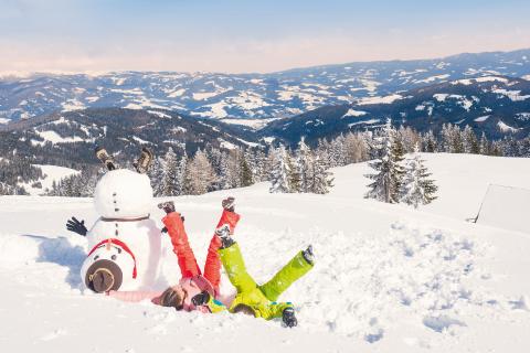 Sie sehen zwei Kinder, die im Schnee spielen neben einen selbstgebauten Schneemann am Klippitztörl