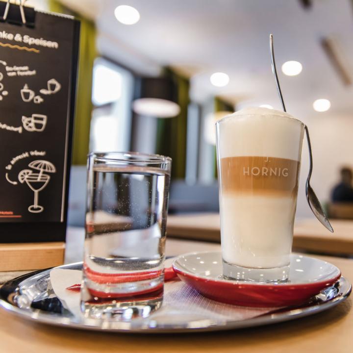 Sie sehen einen Latte Macchiato im gemütlichen Café im JUFA Hotel Schladming. Der Ort für erholsamen Familienurlaub und einen unvergesslichen Winterurlaub.