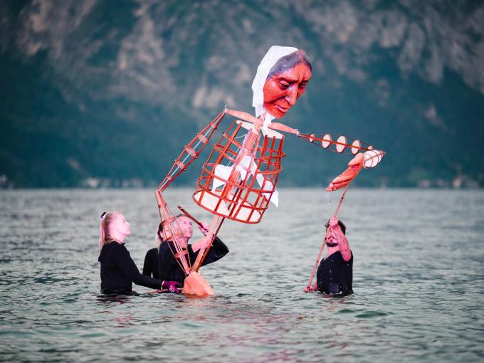 Sie sehen ein Bild von einer rosa-weißen Figur im See, die von mehreren Personen inszeniert wird. Besuchen Sie das Salzkammergut mit der Europäischen Kulturhauptstadt 2024 Bad Ischl.