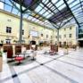 Sie sehen die Innenhof-Lobby mit Bar- und Rezeptionsbereich im JUFA Hotel Wien-City. Der Ort für erholsamen Städteurlaub in Österreich.