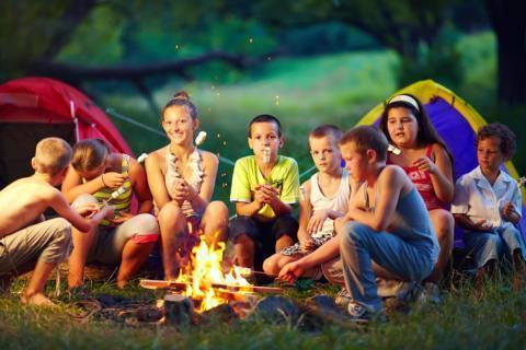 Kinder beim grillen Marshmallows über einem Lagerfeuer in der Natur bei Abendstimmung. JUFA Hotels bietet erlebnisreiche Feriencamps in den Bereichen Sport, Gesundheit, Bildung und Sprachen.