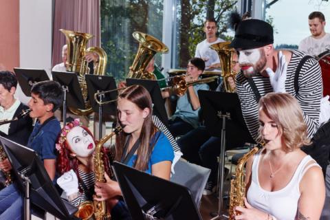 Sie sehen ein Orchester in der Musikakademie Knappenberg mit Pantomimen. JUFA Hotels bietet den idealen Platz zum Musizieren und Singen in der Gemeinschaft in abwechslungsreichen Regionen.