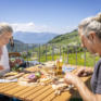 Sie sehen ein Paar beim Essen auf der Terrasse im JUFA Hotel Laterns – Klangholzhus***. Der Ort für erholsamen Familienurlaub und einen unvergesslichen Winter- und Wanderurlaub.