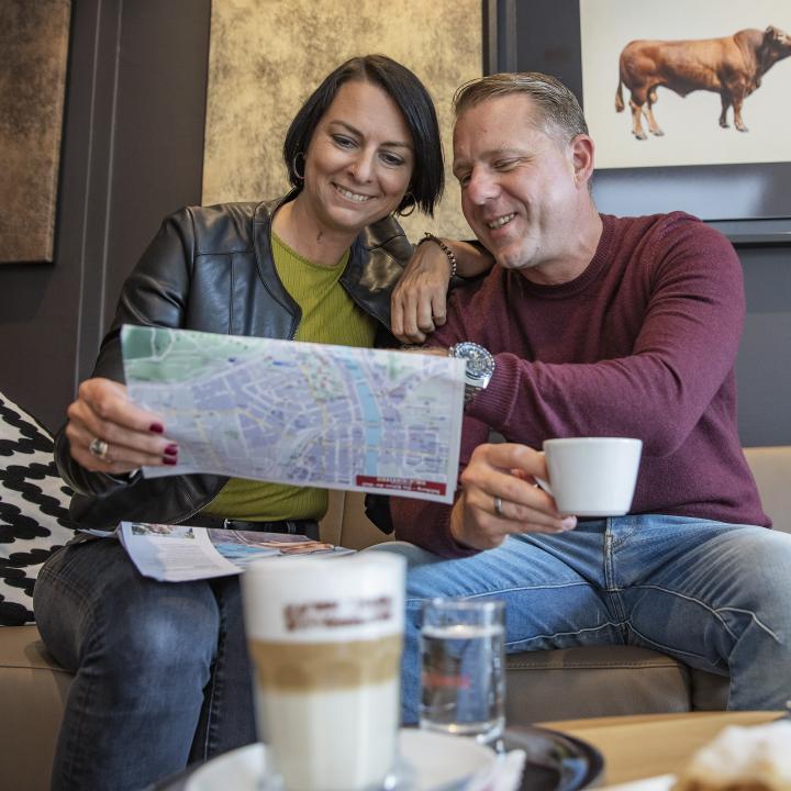 Sie sehen ein Paar mit Kaffee in der Lobby im JUFA Hotel Salzburg City. Der Ort für erholsamen Familienurlaub und einen unvergesslichen Winter- und Wanderurlaub.