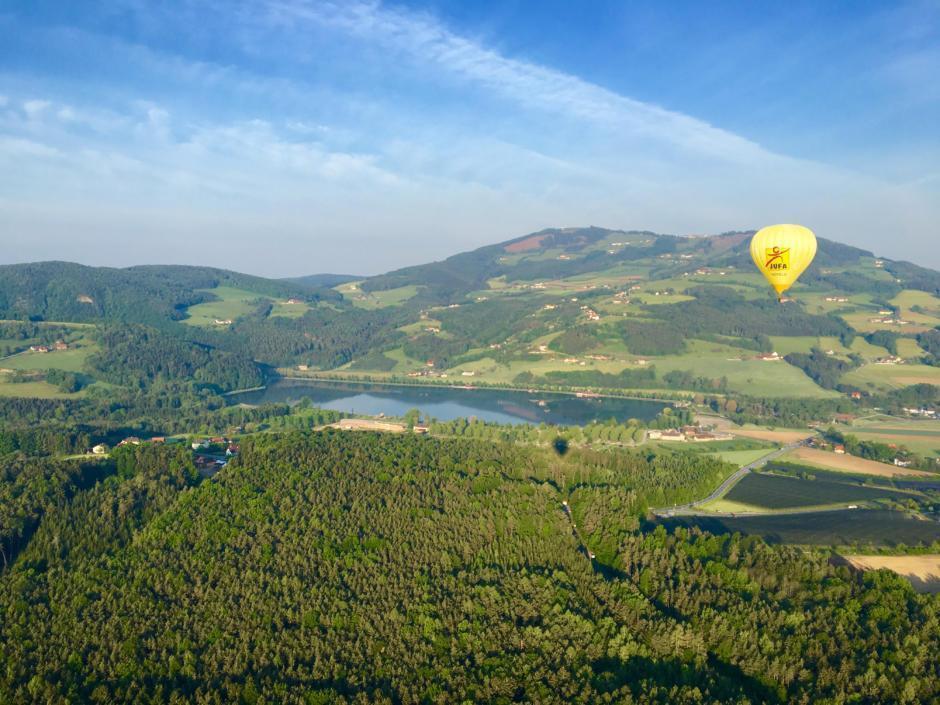 Panoramaaufnahme mit dem JUFA Heißluftballon über der wunderschönen Landschaft in der Nähe vom JUFA Hotel Stubenbergsee. Der Ort für tollen Sommerurlaub an schönen Seen für die ganze Familie.