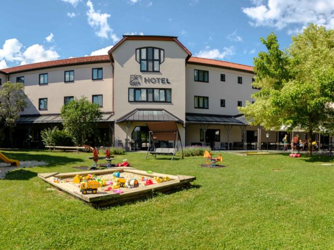 Sie sehen das JUFA Hotel Lipizzanerheimat von Aussen mit Garten und Spielplatz. JUFA Hotels bietet kinderfreundlichen und erlebnisreichen Urlaub für die ganze Familie.