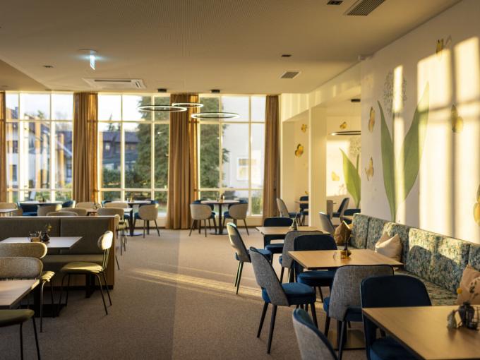 Sie sehen den sonnenlichtdurchstrahlten Restaurantbereich im Café & Restaurant Wandelhalle mit modernen und gemütlichen Sitzmöglichkeiten im JUFA Hotel Bad Radkersburg.