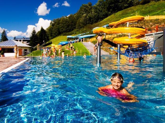 Sie sehen das Freibad Saalbach mit Rutsche im Sommer in der Nähe vom JUFA Alpenhotel Saalbach****. Der Ort für kinderfreundlichen und erlebnisreichen Urlaub für die ganze Familie.