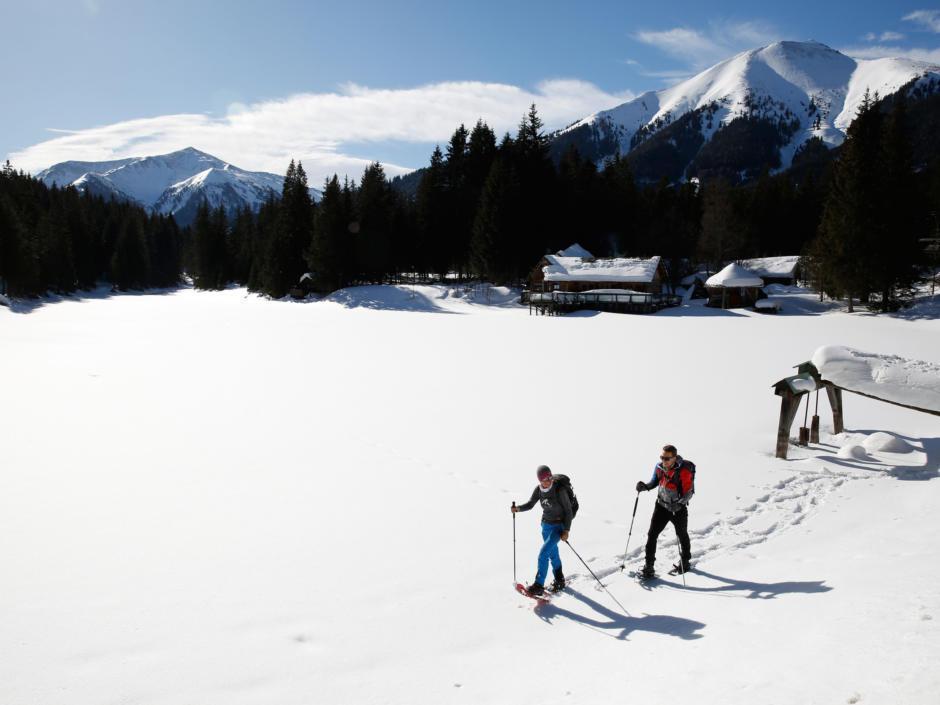 Sie sehen ein Paar beim Schneeschuhwandern bei Sonnenschein im Murtal im Winter. JUFA Hotels bietet erholsamen Familienurlaub und einen unvergesslichen Winterurlaub.