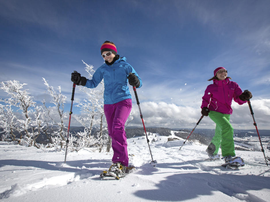 Sie sehen 2 Personen beim Schneeschuhwandern inmitten verschneiter Landschaft im Schwarzwald.