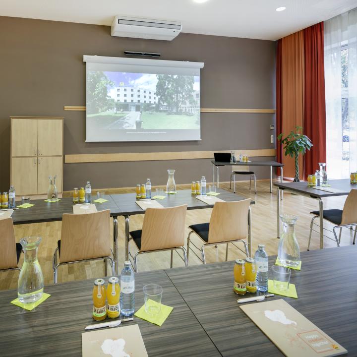 Sie sehen einen Seminarraum mit Beamer-Leinwand im JUFA Hotel Graz City***. Der Ort für erfolgreiche und kreative Seminare in abwechslungsreichen Regionen.