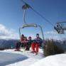 Eine Familie sitzt im Sessellift im Skigebiet Mariazeller Bürgeralpe und genießt einen wunderbaren Skitag. JUFA Hotels bietet erholsamen Familienurlaub und einen unvergesslichen Winterurlaub.